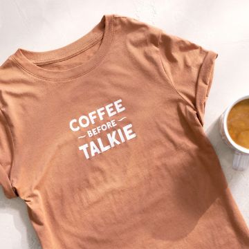 Show details for Day Drinker A light brown t-shirt lies flat on a light surface. The shirt has the words "COFFEE BEFORE TALKIE" printed in white bold letters on the front. Next to the shirt, on the right, is a Chalk Couture transfer filled with coffee.