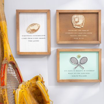 Show details for Sports Quotes Three framed inspirational sports quotes are displayed on a wall. The frames feature quotes from Tom Landry, Babe Ruth, and Serena Williams created with Chalk Couture transfer. To the left, vintage tennis rackets and a baseball glove are leaning against the wall, adding a nostalgic touch.
