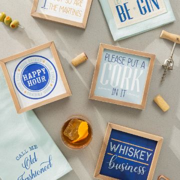 Show details for Call Me Old Fashioned A flat lay of a cocktail-themed scene featuring a whiskey drink with an orange twist, a cocktail skewer with olives, and framed coasters with phrases like "Happy Hour," "Whiskey Business," "Please Put a Cork in It," "Let the Evening Be Gin," and more created using the transfer from Chalk Couture.