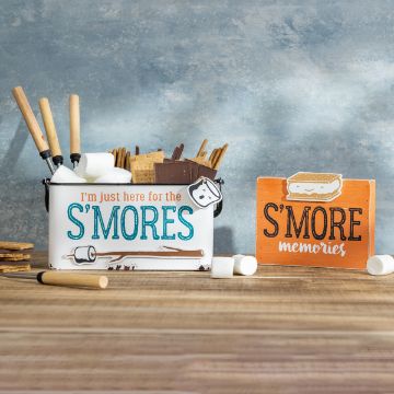 Show details for Outdoors & S'mores Chalkable Shapes (4 Pieces) A container and sign are on a wooden surface. The container holds marshmallows, graham crackers, and chocolate, with the text "I'm just here for the S'MORES" on it. The wooden sign next to it reads "S'MORE memories," with marshmallows scattered around.