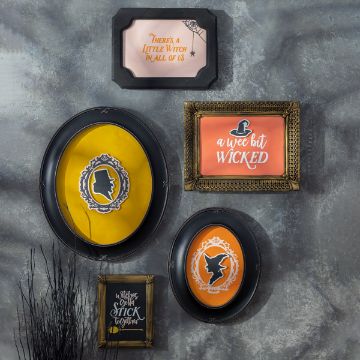 Show details for Couture Boutique® Chalkable Shapes A Wee Bit Wicked (4 Pieces) A collection of five Halloween-themed frames on a textured wall. Each frame features a witch-themed silhouette or quote, such as "There's a little witch in all of us," in ornate frames. Black twigs are visible at the bottom left.