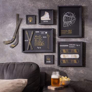 Show details for Snow & Ice Sports A cozy living room features a gallery wall adorned with framed illustrations of winter sports, including skiing, skating, hockey, and snowboarding. A sofa is seen in the foreground with a glass of beer and a bowl of chips placed on an armrest table.