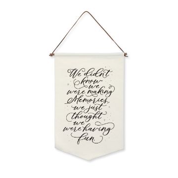 Show details for Black Velvet Ink Single A hanging white banner with a brown cord, displaying handwritten black text that says, "We didn't know we were making memories, we just thought we were having fun." The design includes small black star-like decorations around the lettering. This design uses Ink by Chalk Couture.