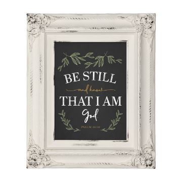 Show details for Sage Paste Single A framed sign with a chalkboard-style background displays the text "Be still and know that I am God" in white and gold, adorned with green leafy designs. The frame is ornate and white with intricate details. Psalm 46:10 is cited at the bottom. Product: Chalk Couture paste