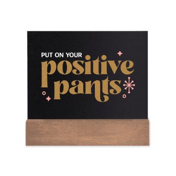 Show details for Shimmer Gold Paste Single A black sign with the text "Put On Your Positive Pants" written in bold, gold letters accompanied by small pink decorative elements. The sign is supported by a simple wooden base. The writing was created using Chalk Couture paste.