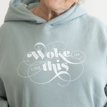 Show details for Woke Up Like This An elderly individual wearing a light blue hoodie with white script text that reads, "I woke up like this." The person is smiling, and the focus is on the upper part of the hoodie and the text, created using a Chalk Couture transfer.