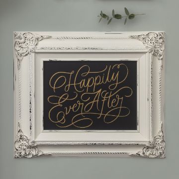 Show details for Ever After A white ornate picture frame against a light gray wall displays the phrase "Happily Ever After" in elegant gold cursive on a black background. A small sprig of greenery is visible at the top right corner, featuring the "transfer" by Chalk Couture.