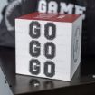 A Chalk Couture transfer with a red top placed on a table, displaying the words "GO GO GO" stacked vertically in black, college-style lettering. The background shows part of a backpack with the word "GAME" visible.
