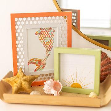 Show details for Under The Sea A small wooden tray holds a starfish, seashells, and two framed pictures. One picture is of a colorful fish with scales, and the other depicts a yellow sun with rays created using the transfer by Chalk Couture. A larger mirror reflects part of the scene in the background.