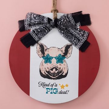 Show details for Kind of a Pig Deal A Chalk Couture transfer features a pig wearing star-shaped blue glasses with the text "Kind of a PIG deal!" written below. The pig is adorned with a black and white patterned bow on a red and white background. The wall decor hangs by a rope on a pink backdrop.