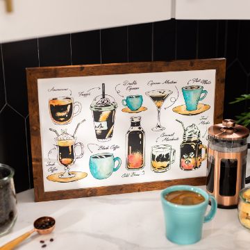 Show details for Coffee Bar A framed poster displays various illustrated coffee drinks with their names: Americano, Frappe, Double Espresso, Espresso Macchiato, Flat White, Irish Coffee, Black Coffee, Iced Mocha, Cold Brew, and Café au Lait. A teal mug and Chalk Couture transfer are on the table.