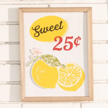 Show details for Fresh Lemonade Chalkable Shapes (3 Pieces) A framed print against a white brick wall featuring a colorful design with the text "Sweet 25¢" above an illustration of a whole lemon, a lemon slice, and a small blossom.