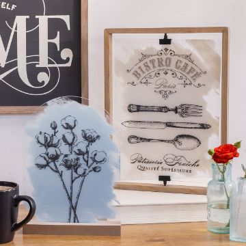 Show details for Floating Frame Bundle (9" x 12") A decorative tabletop setup features framed art pieces: one with "Bistro Café Paris" and vintage cutlery, another with black and white floral art. A fresh red flower in glass vases and a black mug add charm, while a chalkboard art with "ME" is partially visible.