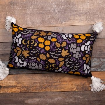 Show details for Spooky Pattern A rectangular black pillow with fringe tassels on the corners lies on a wooden surface. The pillow features a Halloween-themed pattern with ghosts, pumpkins, bats, tombstones, leaves, and moons in orange, white, and gray, set against a dark purple background.