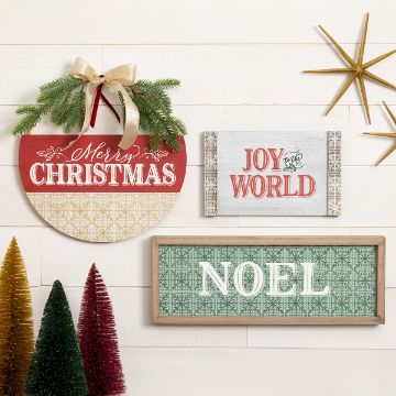 Show details for Merry Christmas Noel A decorated wall with three Christmas-themed signs. The top round sign reads "Merry Christmas" with greenery and a bow. Below are signs that read "Noel" and "Joy to the World." There are also colorful Christmas trees and a golden star decoration.