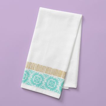 Show details for Tea Towel A neatly folded white tea towel with decorative light blue and yellow patterns along one edge is placed on a pastel purple surface. The design features intricate circular motifs and vertical stripes, giving the towel an elegant and stylish appearance.