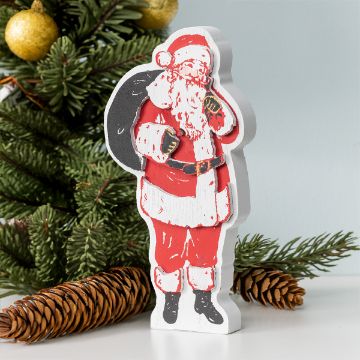Show details for Little Saint Nick A wooden figure painted to resemble Santa Claus holding a sack stands in front of a Christmas tree branch and pine cones. Santa is depicted wearing his traditional red suit with white fur trim and black boots, with a festive background including golden ornaments.