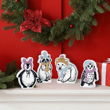 Show details for Cozy Critters (4-Pack) Four illustrated animal holiday decorations are displayed on a mantle with a festive wreath and gift box. The animals, all dressed in winter accessories, include a penguin, a raccoon, a polar bear, and an owl, each wearing scarves, hats, or earmuffs.