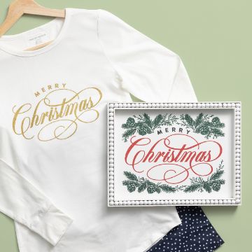 Show details for Merry Christmas & Pine A white long-sleeve shirt with "Merry Christmas" written in gold script is displayed on a hanger. Next to it, there is a framed sign with "Merry Christmas" written in red script, surrounded by green festive foliage. The backdrop is a light green surface.
