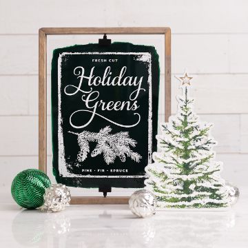 Show details for Pesto Paste Single A festive holiday display featuring a framed sign that reads "Fresh Cut Holiday Greens" with pine branches. Next to it is a standing decorative Christmas tree and three ornaments in green and silver on a light background.
