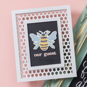 Show details for Shimmer Shadow Paste Single A decorative bee illustration with wings and stripes is centered on a blackboard-like background with the text "our guest." The image is framed by a white honeycomb-patterned frame against a pink surface.