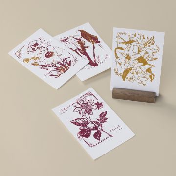 Show details for Base (3½" x 1¼" x ¾" ) Four artistic floral prints on paper: two red and two gold. Each features detailed illustrations of various flowers, placed on a beige surface. One print is upright in a wooden holder.