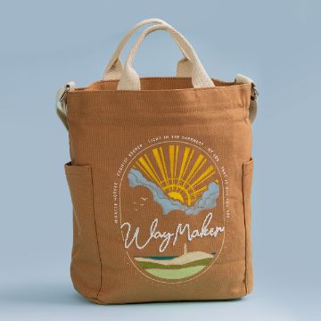 Show details for Way Maker A brown tote bag with beige handles against a light blue background. It features a design of a sunrise over hills with words like "Way Maker," "Miracle Worker," and "Promise Keeper" in white text. Two pockets are on the sides of the bag.