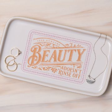Show details for Beauty Doesn't Rinse Off A rectangular tray with decorative text that reads "100% Genuine Beauty Doesn't Rinse Off." The tray holds two pairs of hoop earrings and a necklace with a half-circle pendant. The background is a light wood texture.