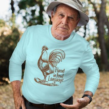 Show details for Fowl Language Elderly man wearing a light blue shirt with a rooster illustration and the text "Fluent in Fowl Language," outdoors in a garden setting with trees in the background.
