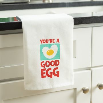 Show details for You're A Good Egg A white kitchen towel hanging on a counter, featuring an illustration of a fried egg with text above and below saying "YOU'RE A GOOD EGG" in bold red letters.