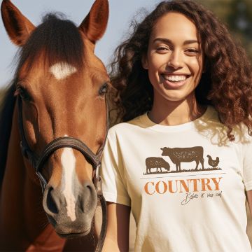 Show details for Country Before It Was Cool A woman smiling broadly stands next to a brown horse. She is wearing a white t-shirt with silhouettes of a cow, sheep, and chicken, and the text "COUNTRY Before it was cool." Sunlight casts a warm glow on her and the horse.