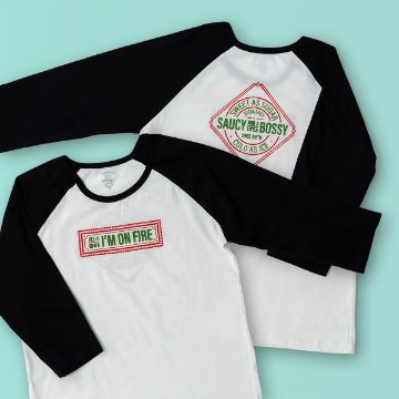 Show details for Sweet As Sugar Two white and black raglan shirts on a teal background. One shirt reads "Hello, I'm on fire," and the other says "Sweet as sugar, saucy and bossy, cold as ice" with decorative borders.