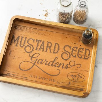 Show details for Mustard Seed Gardens Wooden tray with "Mustard Seed Gardens" and "Faith Grows Here" inscribed on it. Two glass jars with seeds are on and beside the tray. The tray has a rustic and natural design, placed on a light marble surface.
