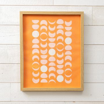 Show details for Moon Phases Framed abstract artwork featuring a pattern of white semi-circles and ovals on an orange background. The frame is a light wood, and the piece is mounted on a white wooden wall.
