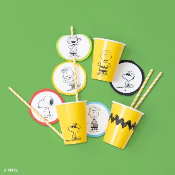 Show details for Peanuts - Classic Minis Yellow paper cups with black zigzag patterns and cartoon characters, with striped straws. Circular cutouts feature illustrations of a dog and children on a green background.
