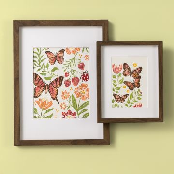 Show details for Butterfly Florals Two framed artworks on a light green wall, featuring colorful butterflies and floral designs. The larger frame has more detailed flowers, while the smaller frame focuses on two butterflies and a few flowers. Both frames have wooden borders.