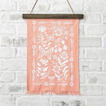 Show details for Butterfly Garden A pink hanging textile with white floral patterns, butterflies, and strawberries. The fabric features fringed edges, and it's mounted on a wooden rod against a white brick wall.
