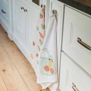Show details for Grow Your Own Kitchen towels with colorful fruit designs hang from cabinet handles. The white cabinets and wood floor create a bright and cozy atmosphere.