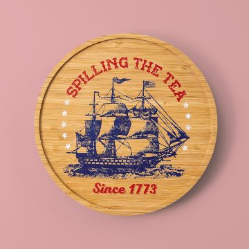 Show details for Spilling The Tea Wooden coaster with a blue ship illustration and decorative text. "SPILLING THE TEA" is written in red at the top, with white stars surrounding it, and "Since 1773" in red at the bottom. The background is a soft pink.