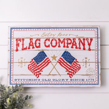 Show details for Flag Company A vintage-style sign with the text "Betsy Ross Flag Company." It features two crossed American flags, a gold star, and additional text "Stitching Old Glory Since 1776." Decorative elements include stars and a border, with greenery in the corner.