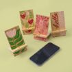 Four decorative wooden phone stands are displayed on a light green background. Each stand features a unique design: red birds, pink abstract pattern, "hello" text, and a green leaf. A smartphone lies face up in front of the stands.