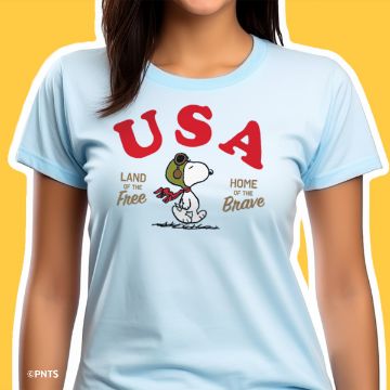 Show details for Peanuts - USA A woman wears a light blue T-shirt with a graphic of Snoopy dressed as a World War I flying ace. Above Snoopy, it says "USA" in red letters. Below, it reads "Land of the Free, Home of the Brave." The background is yellow.