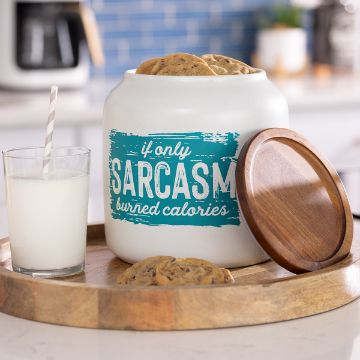 Show details for Sarcasm Burned Calories A glass of milk with a striped straw sits on a wooden tray next to a cookie jar filled with chocolate chip cookies. The jar reads, "If only sarcasm burned calories." The jar’s wooden lid rests beside it.
