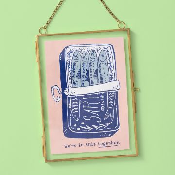 Show details for In This Together A framed illustration of sardines packed in a tin, drawn in blue and white, with the phrase "We're in this together." The frame hangs from a chain against a light green background.