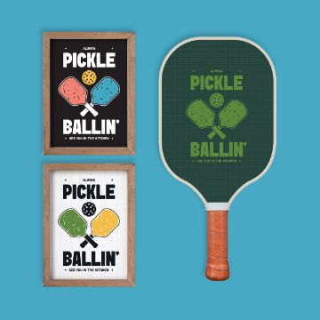 Show details for Pickle Ballin' A green pickleball paddle with "Always Pickle Ballin'" text beside two framed posters featuring colorful paddle graphics and the same slogan, all on a bright blue background.
