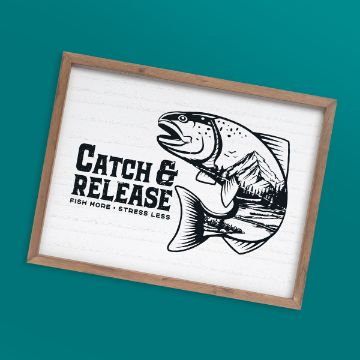 Show details for Catch & Release Framed illustration of a fish with a landscape inside its body and the words "CATCH & RELEASE" and "FISH MORE • STRESS LESS" on a white background, set against a teal surface.