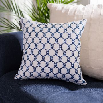 Show details for Nautical Knots Pattern A white decorative pillow with a blue nautical rope pattern rests on a dark blue sofa, next to a cream-colored textured pillow, with green leafy plants in the background.