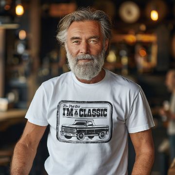 Show details for I'm A Classic A bearded older man with gray hair smiles, wearing a white T-shirt that says "I'm Not Old, I'M A CLASSIC" with a drawing of a vintage pickup truck, standing in a warmly lit, casual indoor setting.