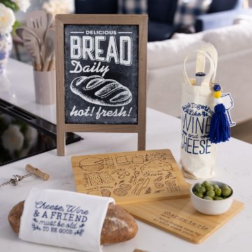 Show details for Daily Bread A kitchen scene with a chalkboard sign reading “Delicious Bread Daily, hot! fresh!” surrounded by a loaf of bread, a cheese board, a small bowl of olives, and a wine bottle in a decorative bag.