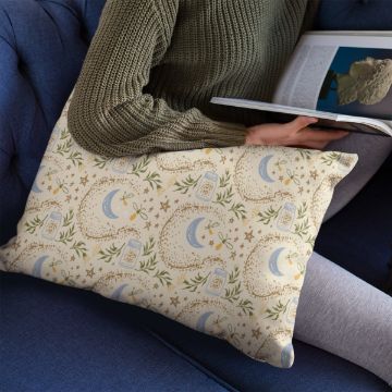 Show details for Firefly Fantasy A person in a green sweater and gray pants sits on a blue sofa, reading a book, with a cream-colored pillow featuring moon, star, and plant patterns resting on their lap.